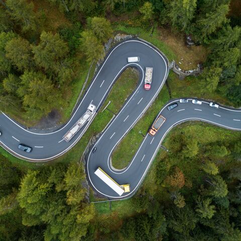 Les voitures roulent sur une route sinueuse avec des arbres au bord de la chaussée.