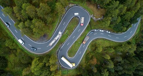 Les voitures roulent sur une route sinueuse avec des arbres au bord de la chaussée.
