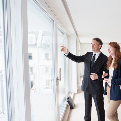 Una giovane coppia si trova in un appartamento vuoto insieme a un agente immobiliare. Tutti e tre guardano sorridendo in direzione della grande finestra.