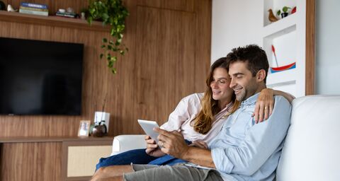 Un couple assis sur un canapé dans le séjour, penché sur une tablette.