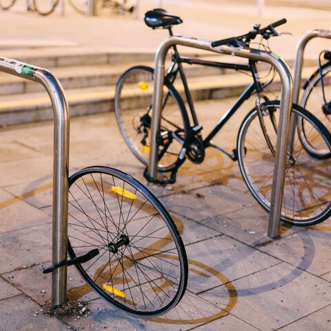 Mehrere Fahrräder sind an einem Fahrradständer angeschlossen, eines davon hat ein fehlendes Vorderrad, das daneben auf dem Boden liegt.