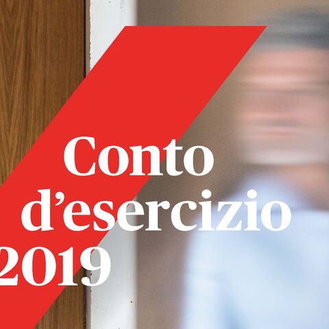 Un uomo con barba e camicia blu si appoggia a una parete di legno e guarda in lontananza. Una striscia rossa con la scritta «Conto d’esercizio 2019» sovrasta l’immagine.