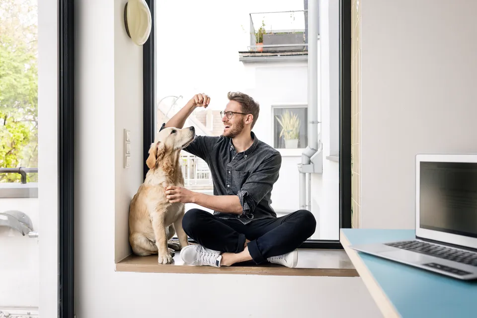 A man is sitting on the floor with his dog and giving it a treat.