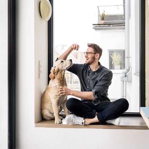 A man is sitting on the floor with his dog and giving it a treat.