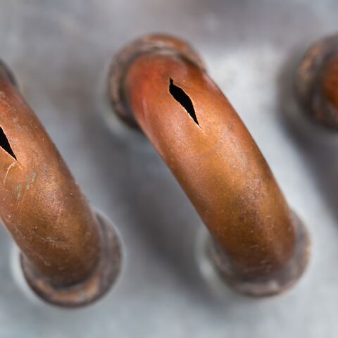 Trois tubes de cuivre rouillés avec des fissures au milieu sur une surface grise.
