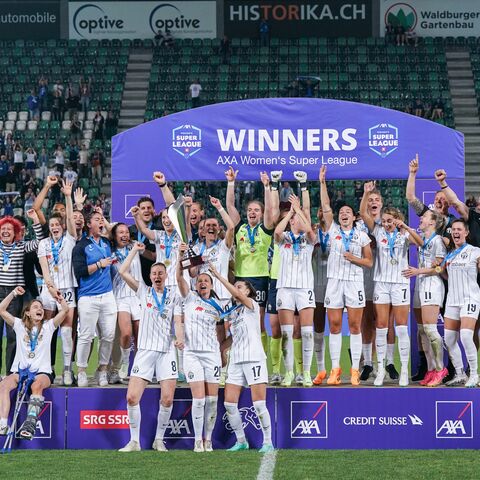 Das Siegerteam der AXA Women's Super League feiert jubelnd vor einem lila Banner mit Medaillen um den Hals und Pokal in der Hand.
