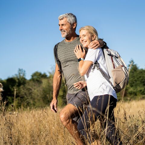 A mature couple walks arm in arm across an autumn meadow.