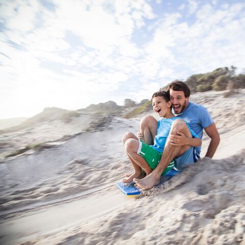 Ein Vater und sein Sohn schlitteln auf einer Sanddüne.