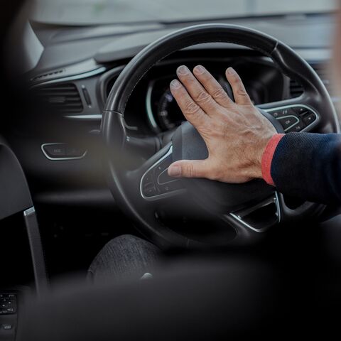 Eine Hand drückt auf die Hupe eines Steuerrades im Auto.