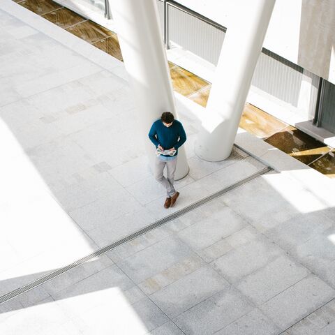 A person stands alone in a large, modern, bright atrium with tall white pillars, reading a book.