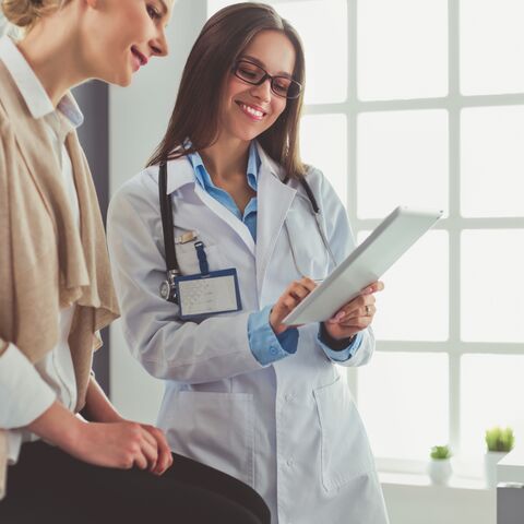Une femme souriante, vêtue d'une tenue médicale bleue et d'une cagoule, qui regarde aimablement au loin.