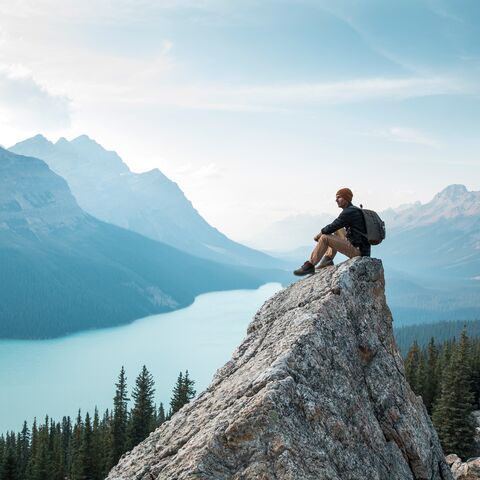 Ein Wanderer mit Rucksack auf dem Rücken, sitzt auf einem Felsen in Kanada. 