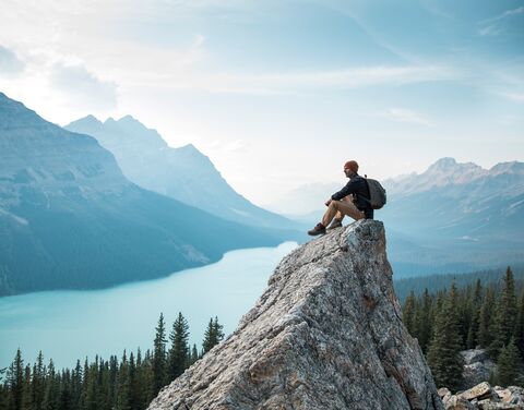 Ein Wanderer mit Rucksack auf dem Rücken, sitzt auf einem Felsen in Kanada. 