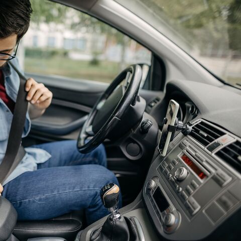 A young man wearing glasses and a beard buckles up in his car.