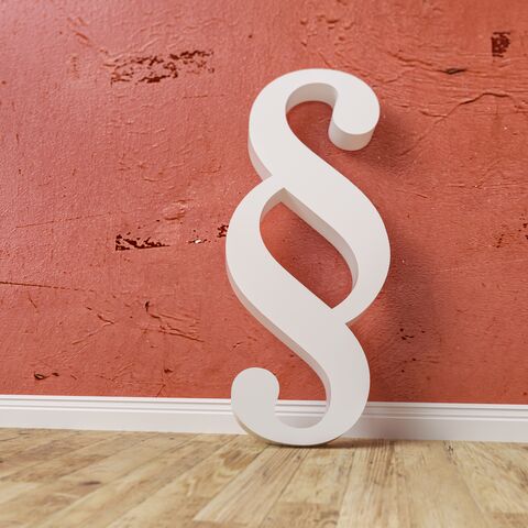 Ein weißes Absatzsymbol steht vor einer roten, strukturierten Wand und ist teilweise vom Bildrand abgeschnitten.