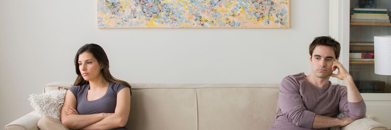 Une femme et un homme sont assis éloignés l’un de l’autre sur un canapé et regardent dans des directions opposées.