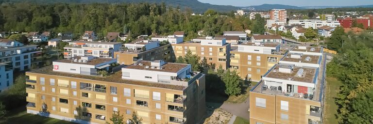 Vue aérienne de plusieurs immeubles résidentiels modernes dans un environnement verdoyant avec des arbres et des pelouses traversées de chemins.
