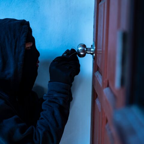 Une personne masquée manipule une serrure avec un fil de fer.