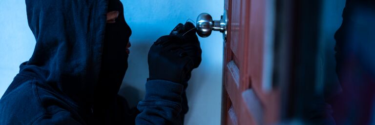 Une personne masquée manipule une serrure avec un fil de fer.