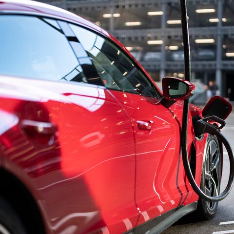 Un’auto elettrica rossa viene ricaricata a una stazione di ricarica e il cavo è inserito nella presa di ricarica sul lato del veicolo.