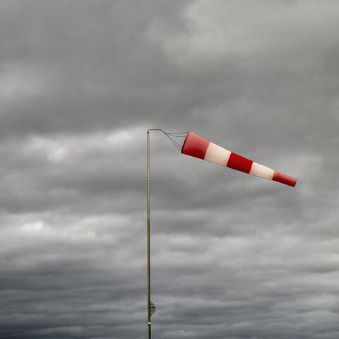 A red-and-white striped windsack blows strongly in a horizontal position against a background of dense, grey clouds in the sky.
