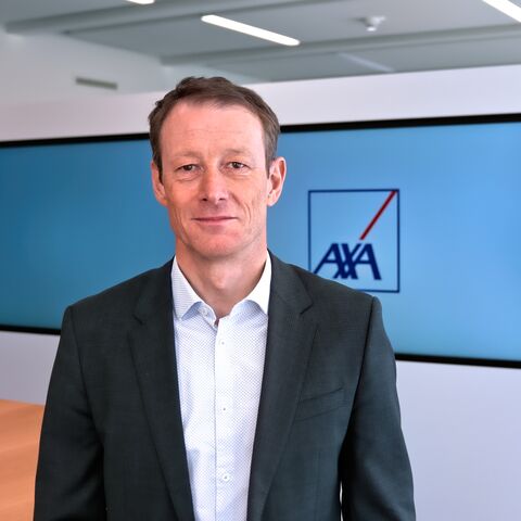 Das Bild zeigt einen Mann der vor drei grossen Bildschirmen steht. Auf dem mittleren Bildschirm steht ein AXA Logo.