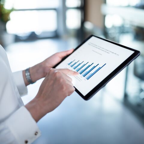 Une personne tient une tablette et analyse un diagramme avec des barres bleues montrant différents points de données.