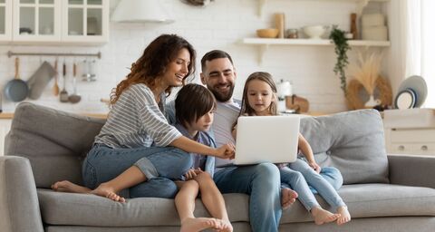 Une famille souriante est assise sur un canapé et regarde un ordinateur portable. Tout le monde semble joyeux et passe du temps ensemble dans un salon confortable.