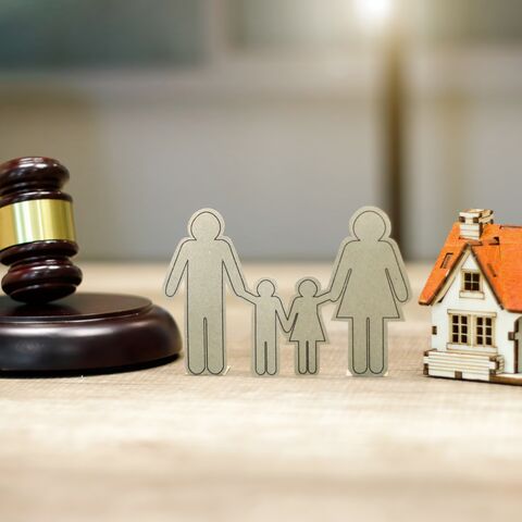 Un marteau, une famille de cartons et une maison sont posés sur une table en bois. 