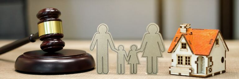 Un martello, una famiglia di cartoni e una casa sono appoggiati su un tavolo di legno. 