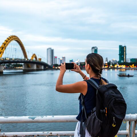 Junge Frau mit einem grossen Rucksack auf dem Rücken, macht mit Ihrem Handy ein Foto von einer Bücke in Vietnam.