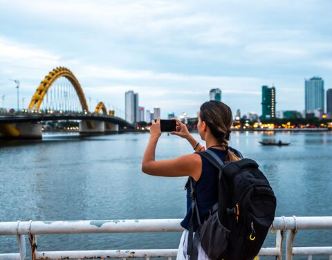 Junge Frau mit einem grossen Rucksack auf dem Rücken, macht mit Ihrem Handy ein Foto von einer Bücke in Vietnam.