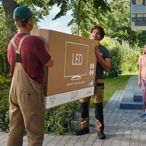 Eine Familie mitten im Umzug steht vor ihrem neuen Haus und bekommt Hilfe von zwei Umzugsmitarbeitern.