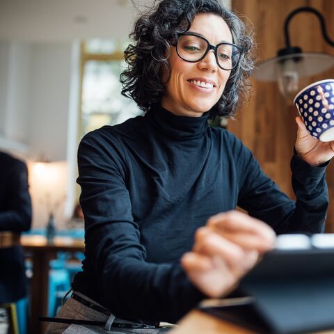 Une femme est assise dans un café, lit ses e-mails et boit du café.