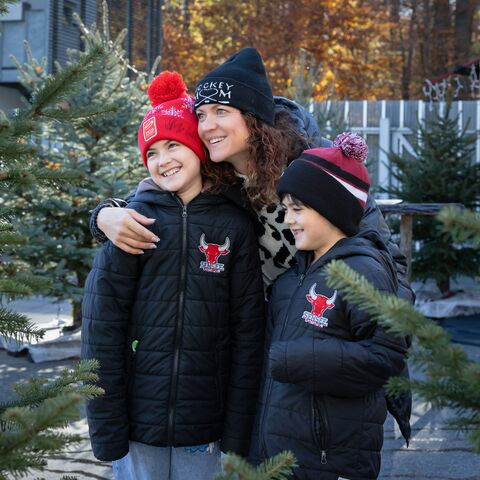 Une mère célibataire avec ses deux enfants, entourée de sapins. Ils portent des vêtements d’hiver.