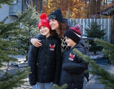 Eine alleinerziehende Mutter mit ihren beiden Kindern, umgeben von Tannenbäumen. Sie tragen Winterkleider.