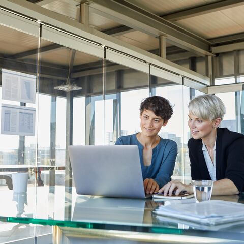 Zwei Frauen sitzen in einem Büro vor einem Laptop und beraten sich.