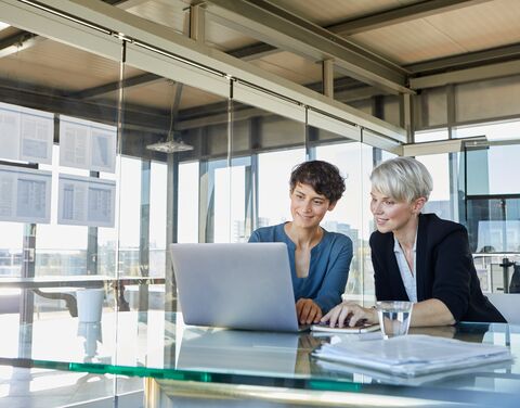 Due donne sono sedute in un ufficio davanti a un laptop e si consultano.