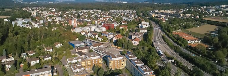 Vue aérienne d’un quartier résidentiel avec plusieurs immeubles d’habitation, entourés d’arbres et de routes, et d’une autoroute en arrière-plan.