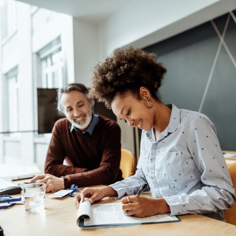 Una donna e un uomo stanno lavorando a una scrivania e sorridono, circondati da materiale da ufficio e un laptop in un ufficio moderno.