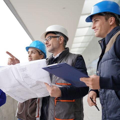 Un gruppo di quattro operai edili con caschi blu e bianchi osserva e discute i piani di costruzione in un cantiere.