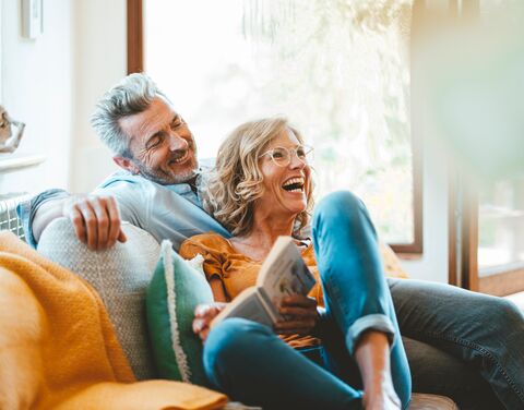 An older couple laughs and cuddles on the sofa in their living room.