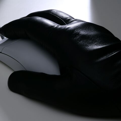 Une main vêtue d'un gant de cuir noir utilise une souris d'ordinateur filaire sur une table blanche.