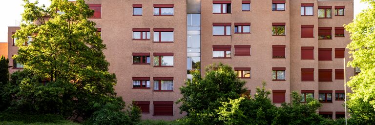 Ein ockerfarbener Wohnblock, davor eine grüne Wiese mit einigen Bäumen