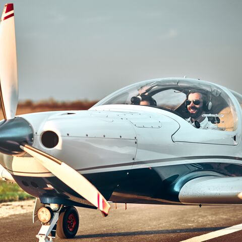 Un pilota con occhiali da sole è seduto in un piccolo aereo monomotore, pronto a decollare in una giornata di sole.