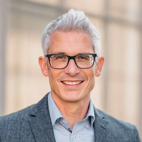 Das Bild zeigt einen lächlnden Mann mit Brille und blauem Anzug.  La photo montre un homme souriant avec des lunettes et un costume bleu.  La foto mostra un uomo sorridente con gli occhiali e un abito blu.  The picture shows a smiling man wearing glasses and a blue suit.