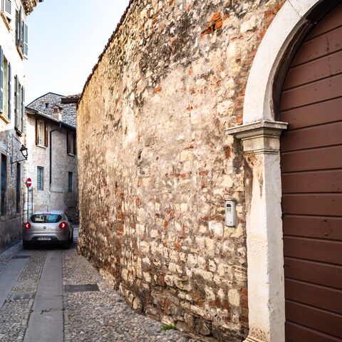A silver car drives through a narrow alleyway of an old town.