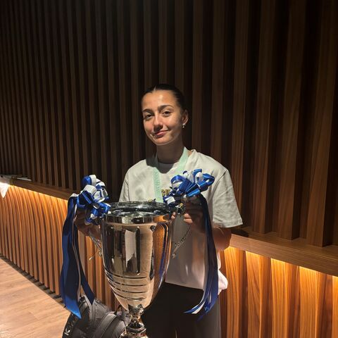 Una giovane calciatrice sicura di sé tiene in mano con un sorriso la coppa.