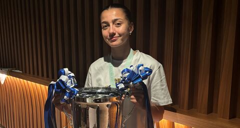 Una giovane calciatrice sicura di sé tiene in mano con un sorriso la coppa.