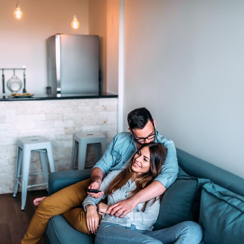 A young couple sits cuddly on the sofa watching TV.